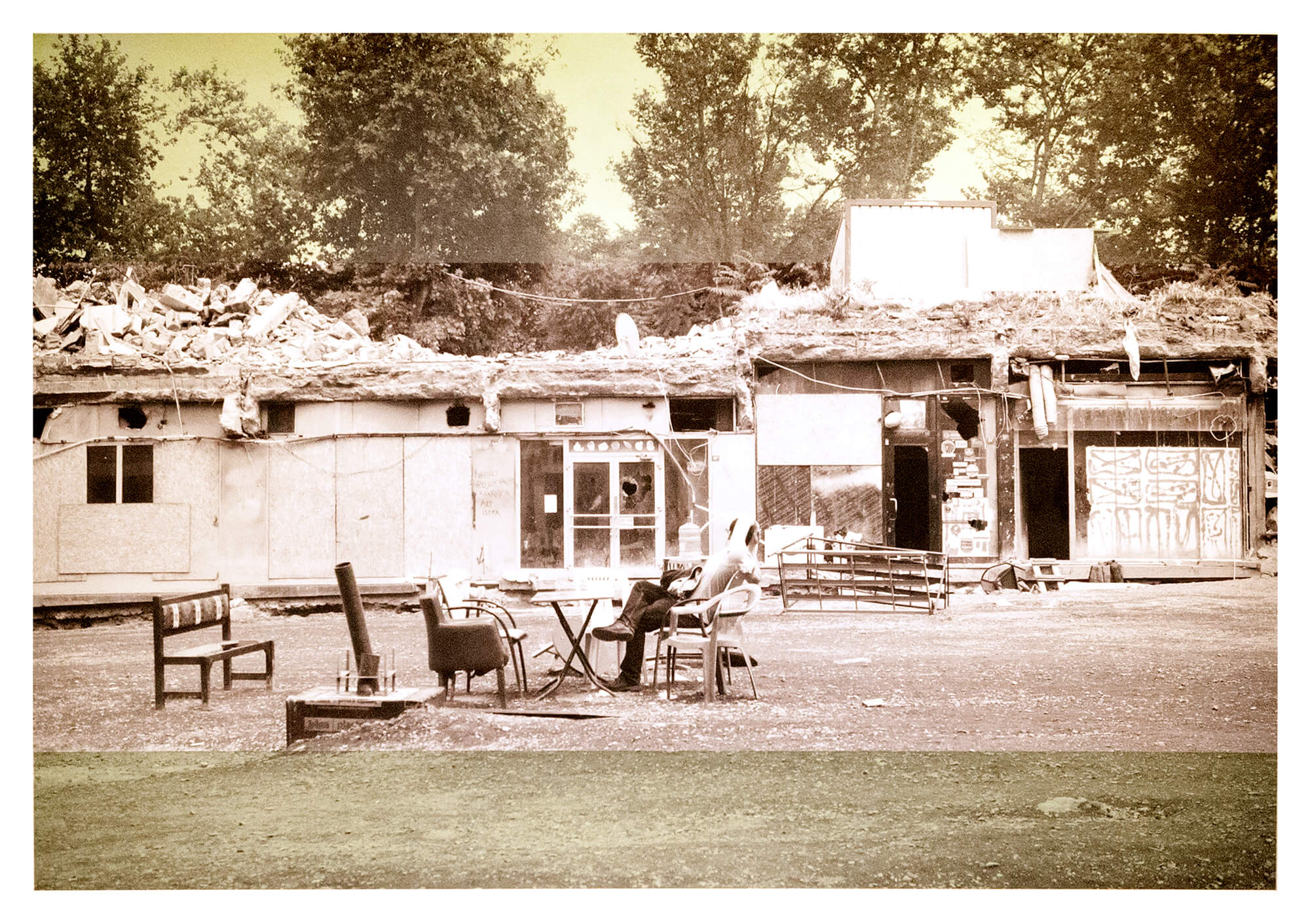 A photo depicting a person relaxing in chair in front of derelict housing