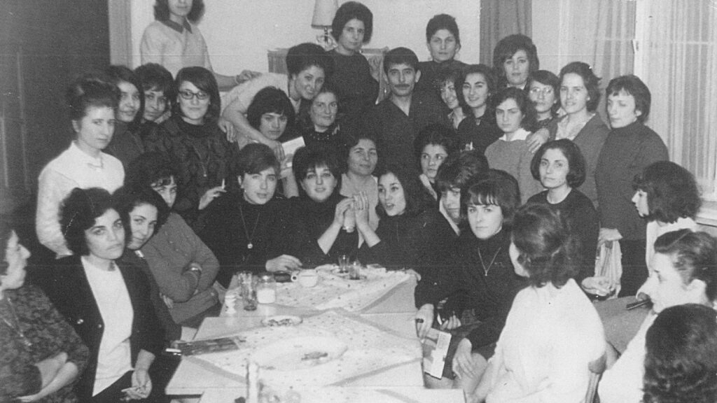 Yemek masasının etrafında poz veren yaklaşık 20 kadını gösteren siyah beyaz bir fotoğraf.