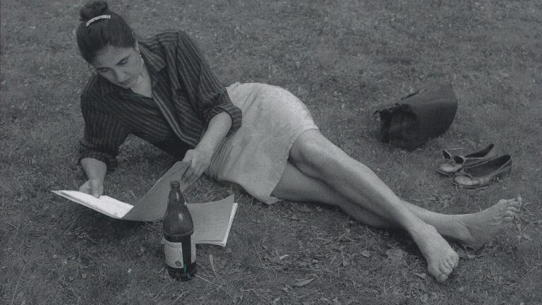 A woman with her shoes off laying on the grass and reading, black and white photo.