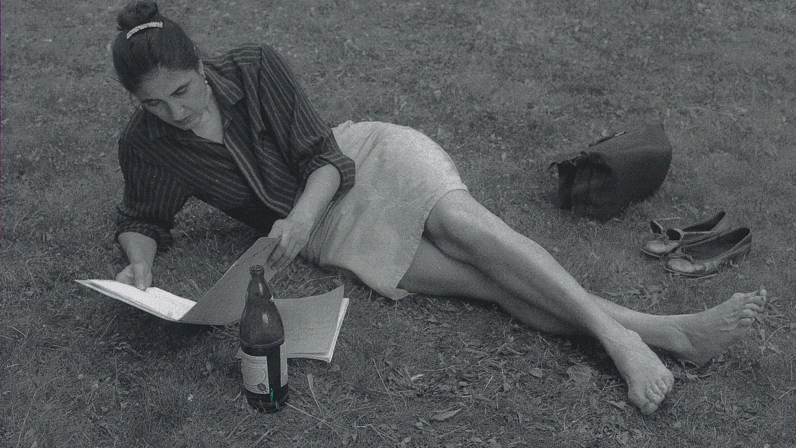 A woman with her shoes off laying on the grass and reading, black and white photo.