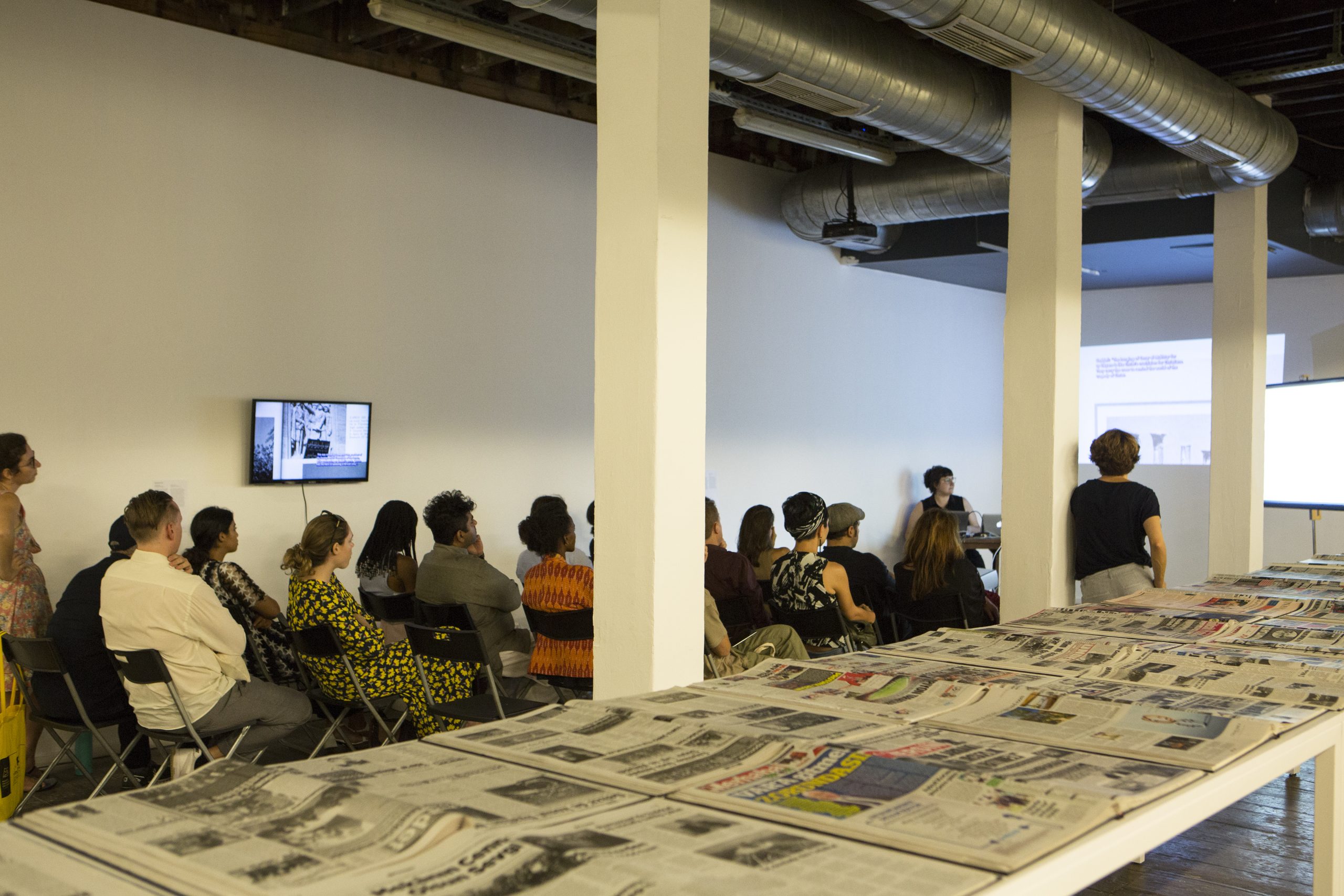 Photo: Exhibition view, people sitting watching the presentation