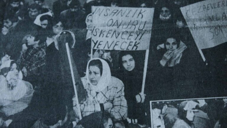 A black and white photo from 1980's portraying a large group of women holding banners and protesting in public space