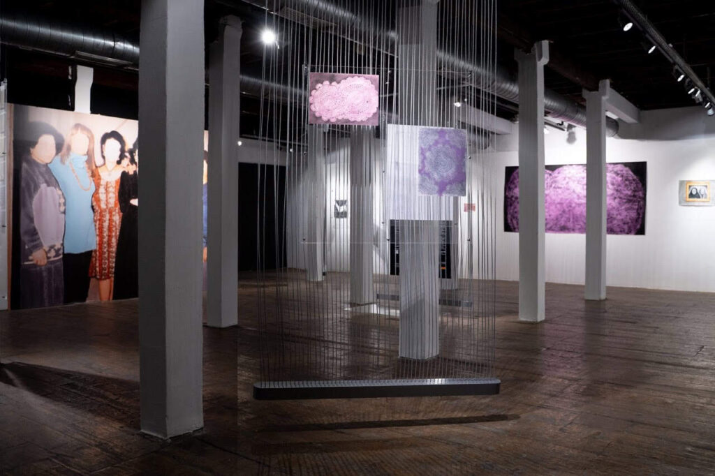 Turkish A photo of exhibition space portraying two abstract artworks hanging on strings up front with larger paintings on the wall behind