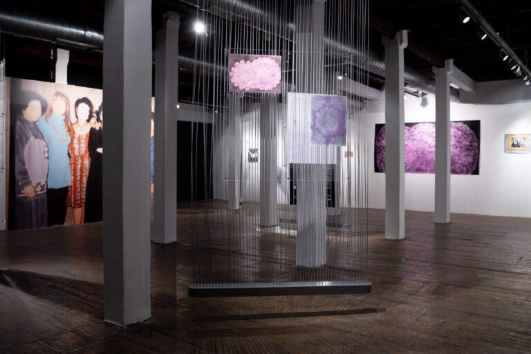 Turkish A photo of exhibition space portraying two abstract artworks hanging on strings up front with larger paintings on the wall behind