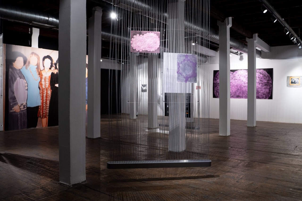 Turkish A photo of exhibition space portraying two abstract artworks hanging on strings up front with larger paintings on the wall behind