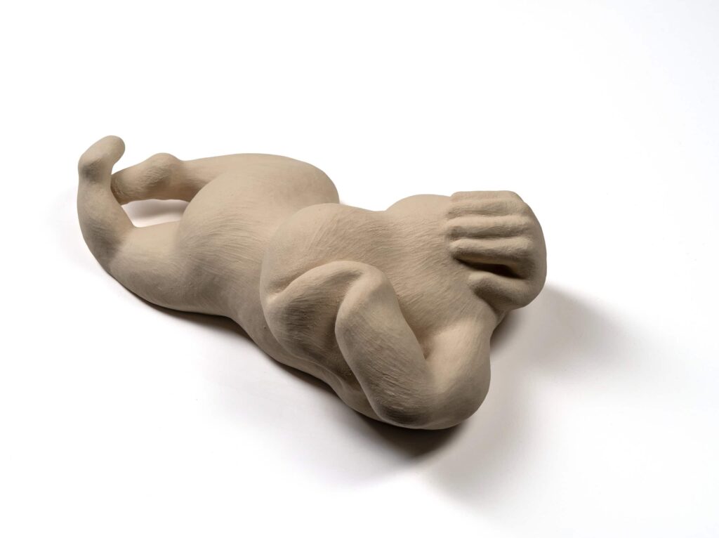Artwork / clay sculpture displaying the stylized human body laying on the floor with hands covering the head, white background